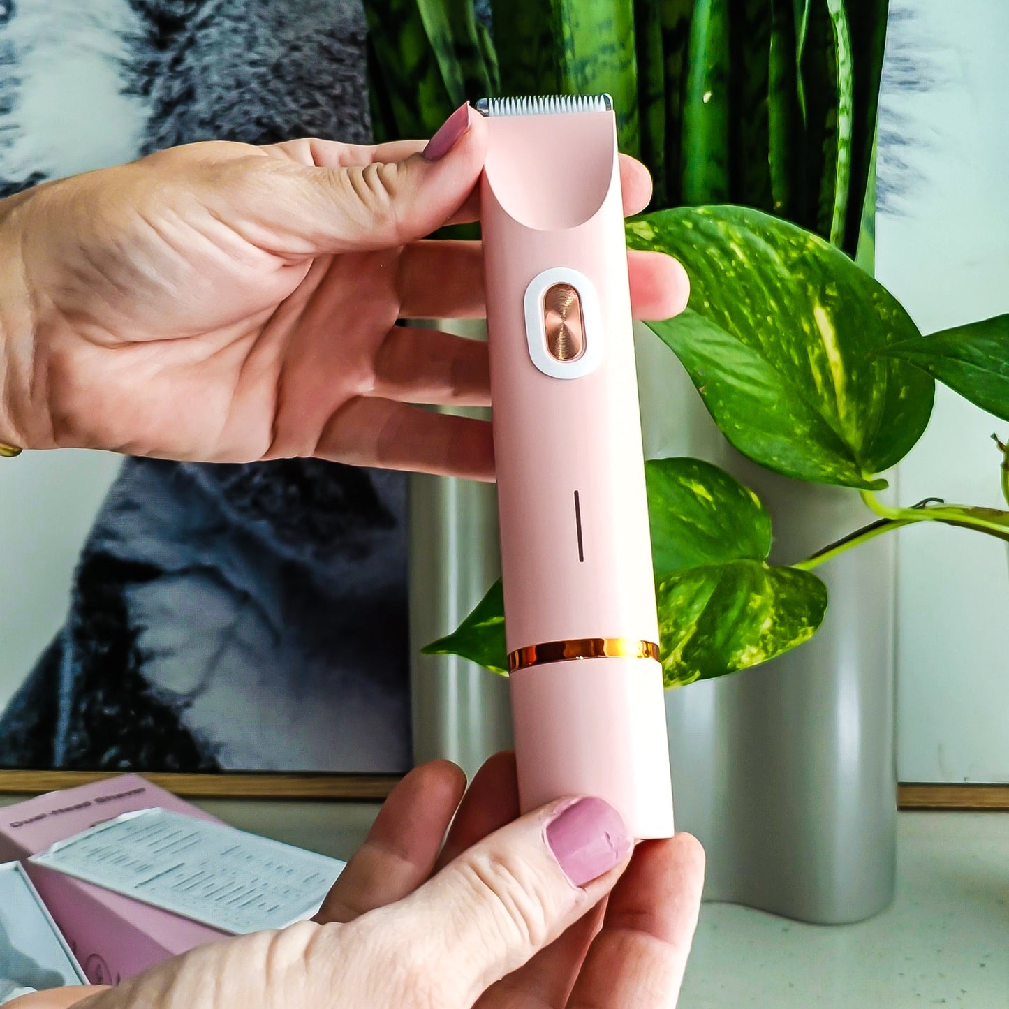 Hand holding a pink electronic device with green plants in the background